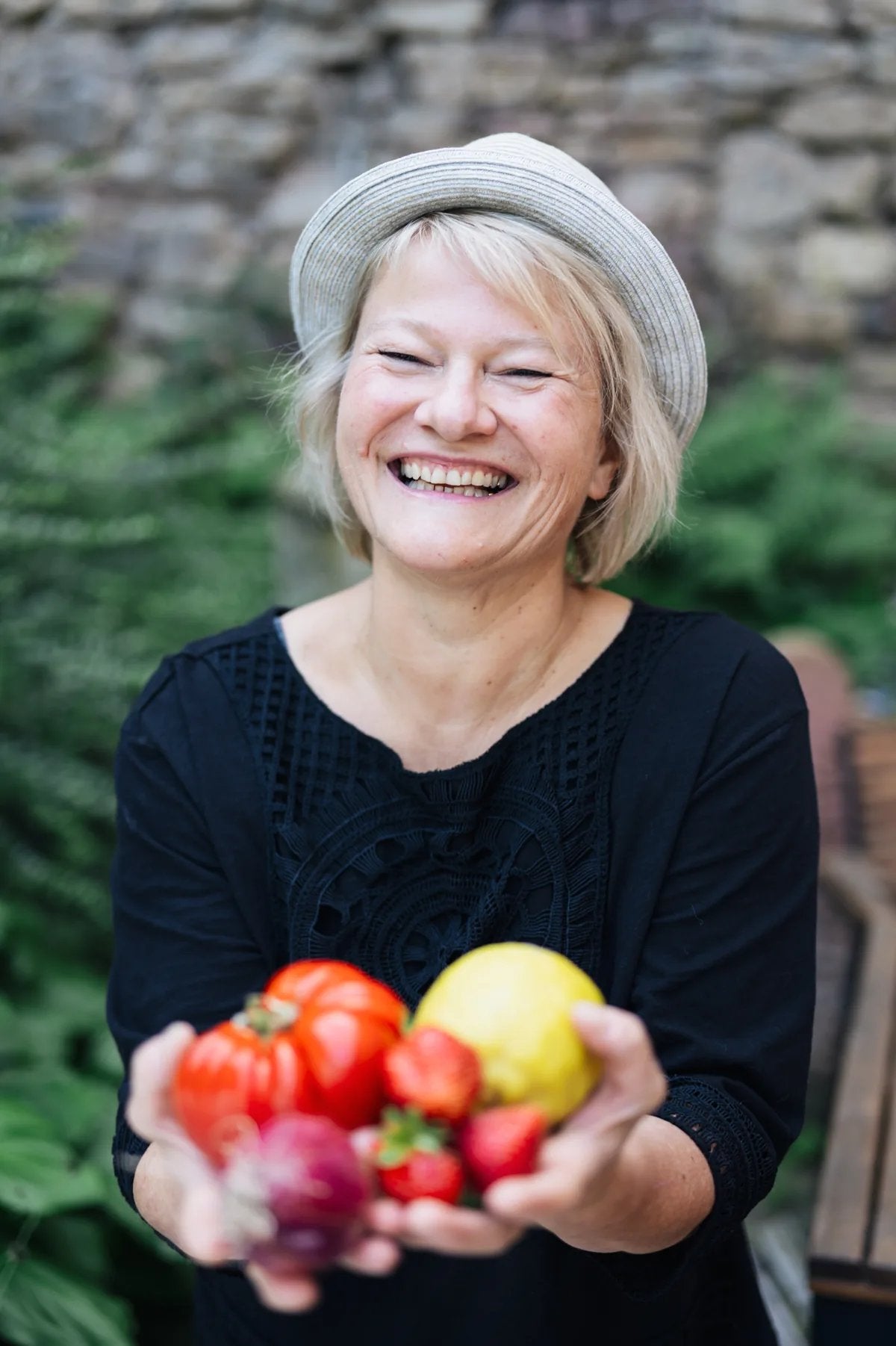 Sylvia Maria Brielmaier, Gründerin der Kompotterie, lächelt und hält frische Tomaten, Erdbeeren und eine Zitrone in den Händen