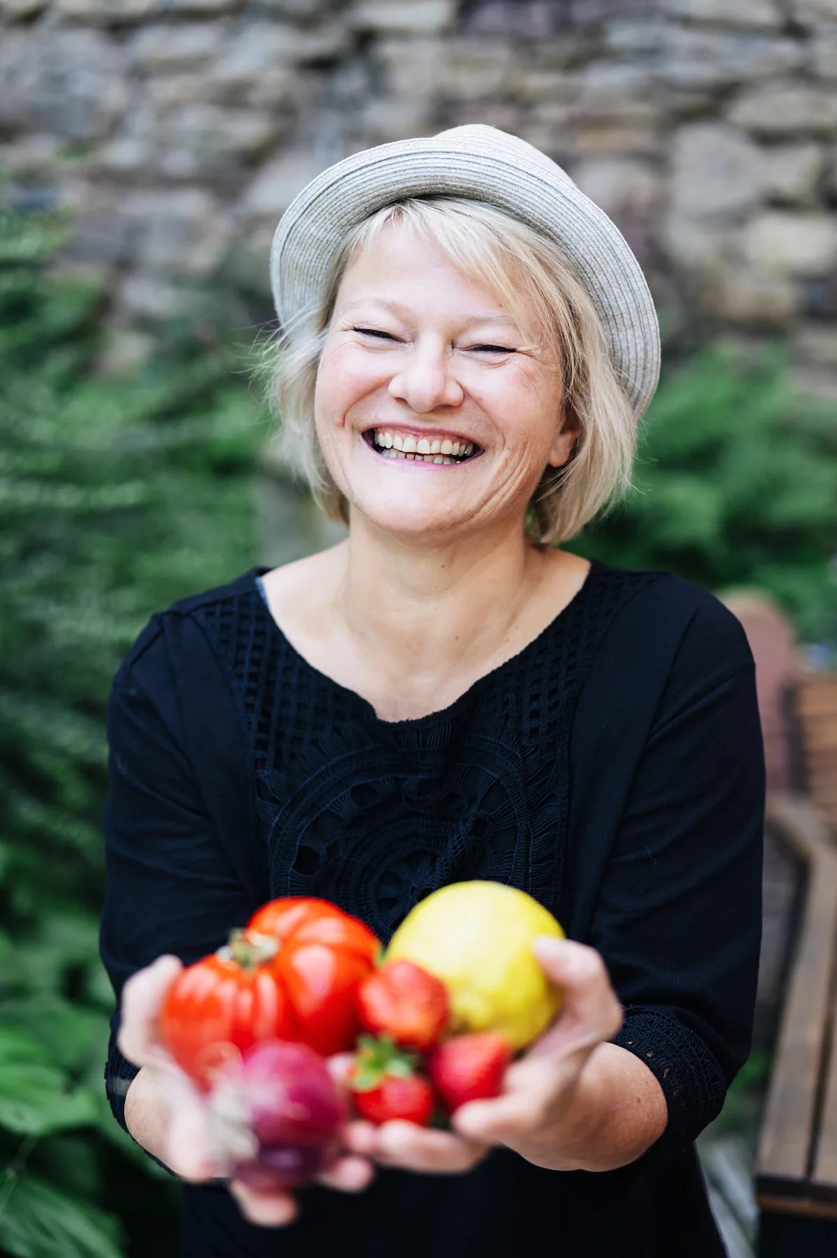 Sylvia Maria Brielmaier, Gründerin der Kompotterie, lacht und hält frische Tomaten, Erdbeeren und eine Zitrone in den Händen
