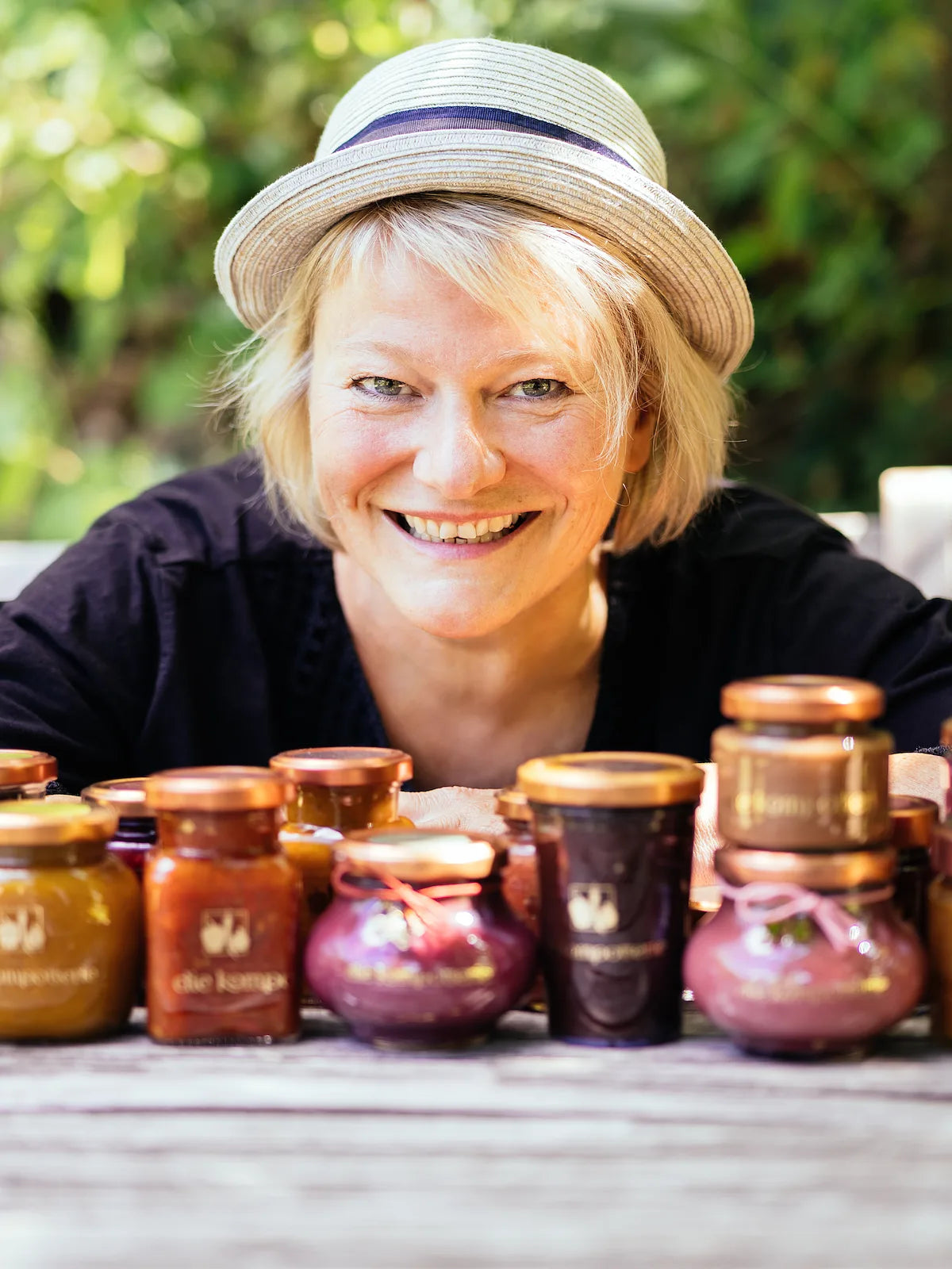 Sylvia Maria Brielmaier hinter einer bunten Auswahl an Curds, Chutneys und Fruchtaufstrichen der Kompotterie auf einem Gartentisch